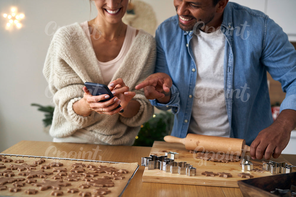 Close up of multi ethnicity couple making a gingerbreads and using mobile phone in Christmas time 