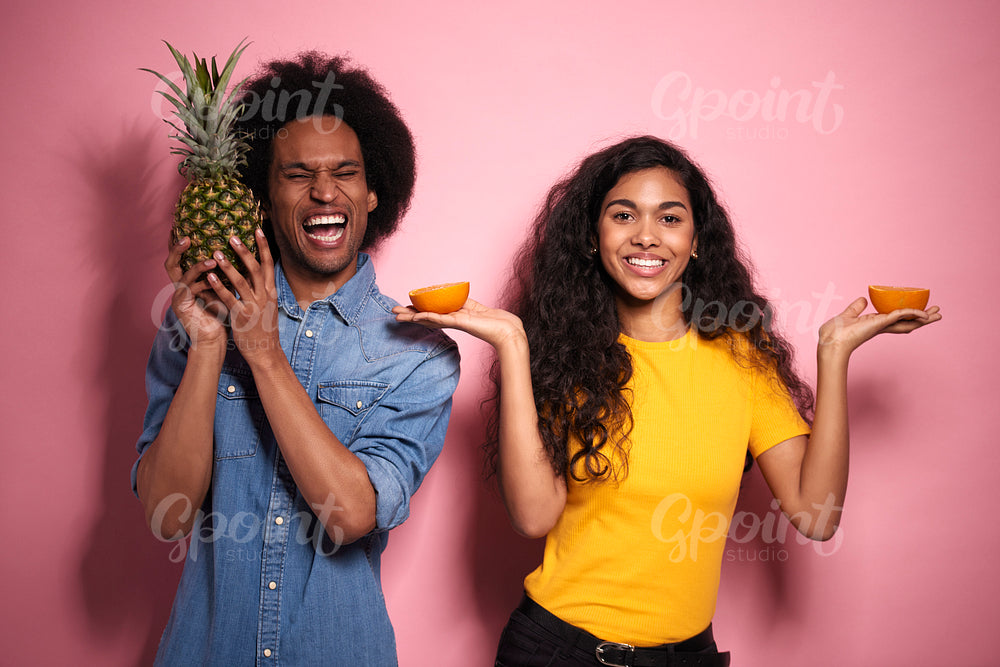 African couple having fun with exotic fruits in studio shot.