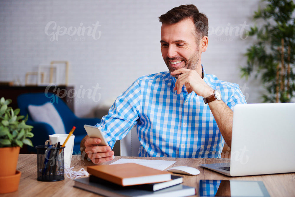 Smiling entrepreneur using mobile phone in his office