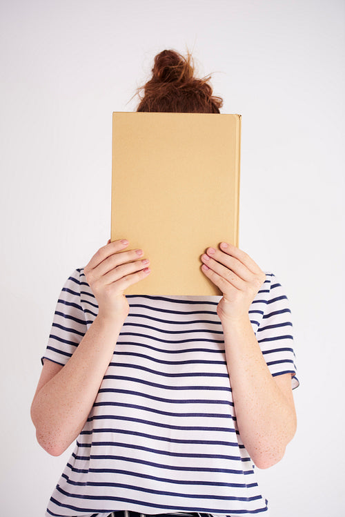 Young woman covering her face with book at studio shot