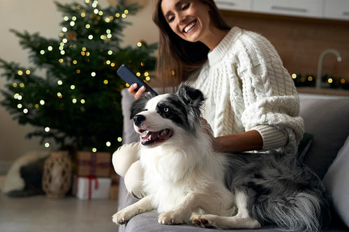 Woman with dog chilling at the sofa with mobile phone during the Christmas