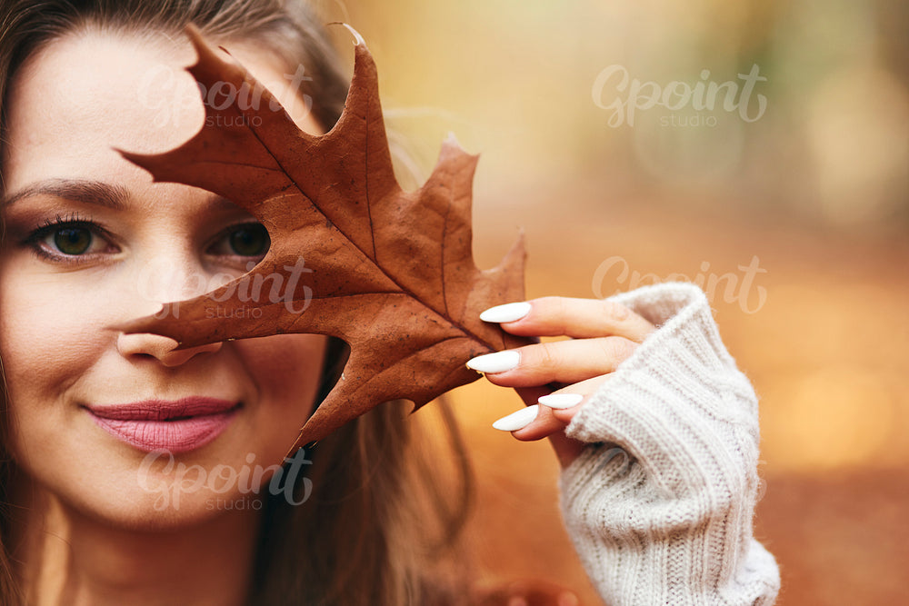 Beautiful woman covering her face with autumn leaves