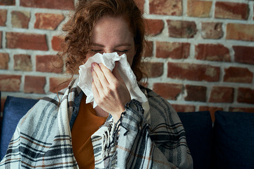 Caucasian woman blowing nose into tissue at home