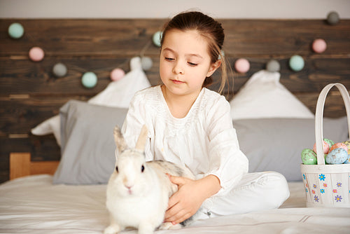 Girl and rabbit sitting on bed