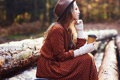 Side view of beautiful woman drinking coffee in autumn forest