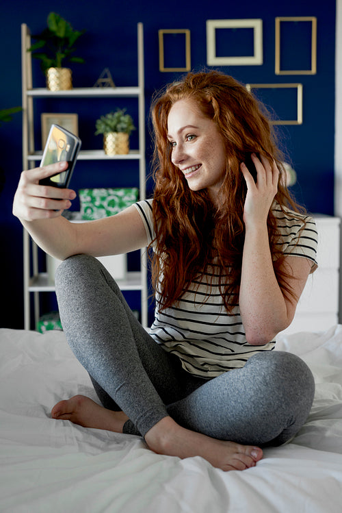 Vertical image of woman taking a selfie on bed