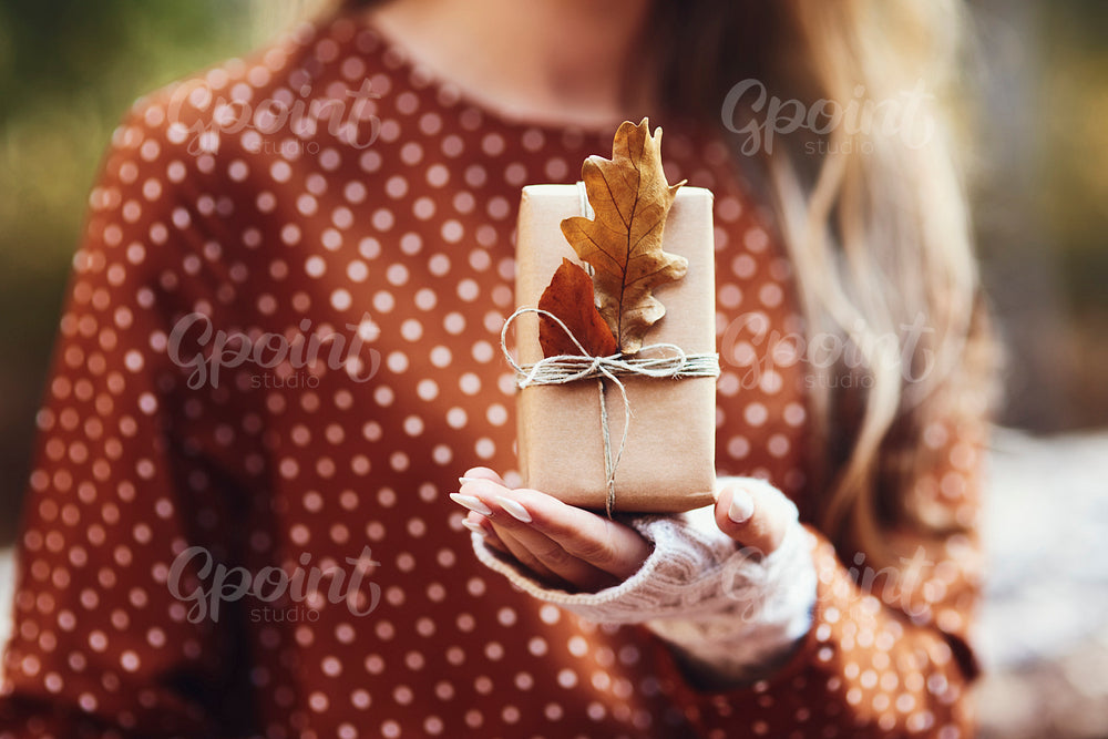 Woman’s hand holding gift wit autumnal leaf