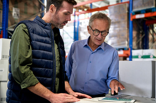 Two caucasian men in mature age discussing over digital tablet in warehouse