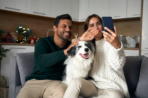 Happy couple with dog talking by video call in Christmas