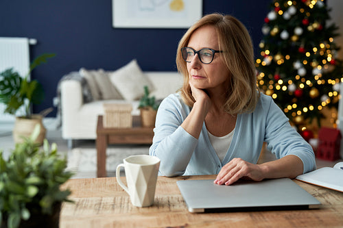 Worried mature woman sitting in front of laptop at home.