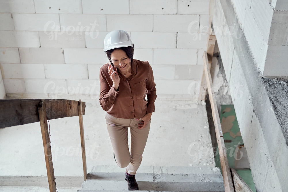 Female mature caucasian engineer moving on the stairs on construction site and talking one mobile phone 