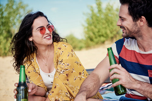 Smiling couple drinking cold beer on the beach