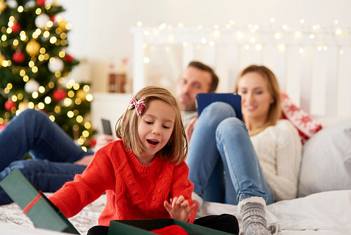 Child opening gift and parents with technology in the background