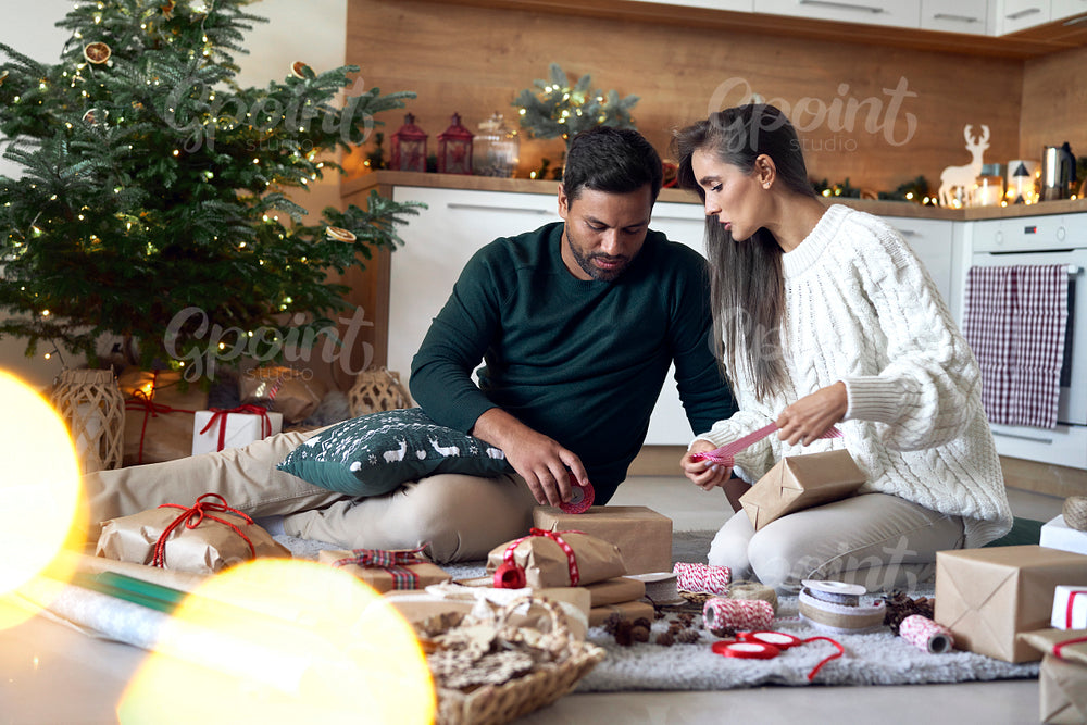 Multi ethnicity couple packing Christmas present together at home 