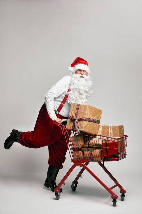 Caucasian Santa Claus pulling shopping cart full of Christmas's presents