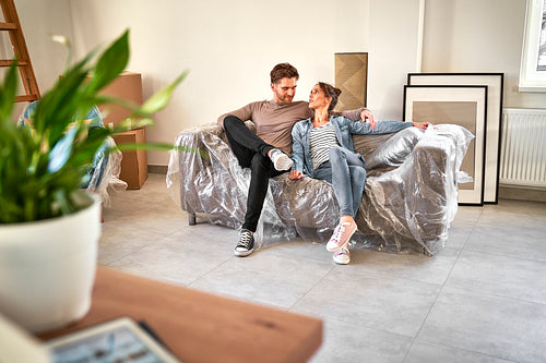 Happy caucasian couple sitting on sofa while moving house