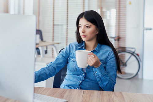 Asian woman drinking coffee and working on computer