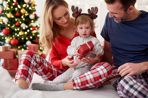 Baby opening Christmas gift with parents in bed