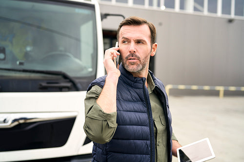 Caucasian mature man in front of warehouse talking by mobile phone