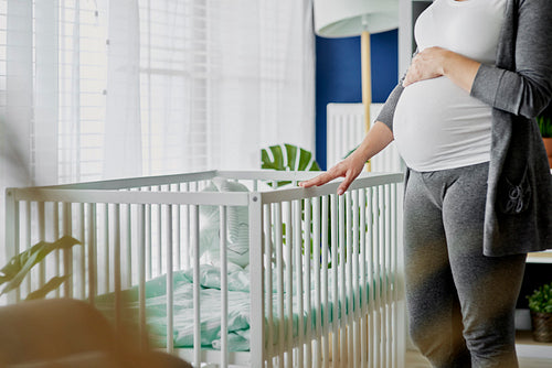 Pregnant woman standing next to a crib