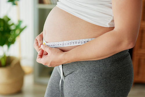 Pregnant woman using tape measure to control the abdomen