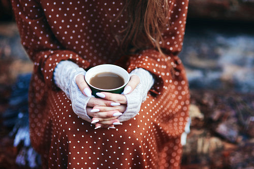 Unrecognizable woman holding a cup of coffee in autumn forest