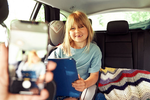 Little girl in car with tablet smiling for the picture