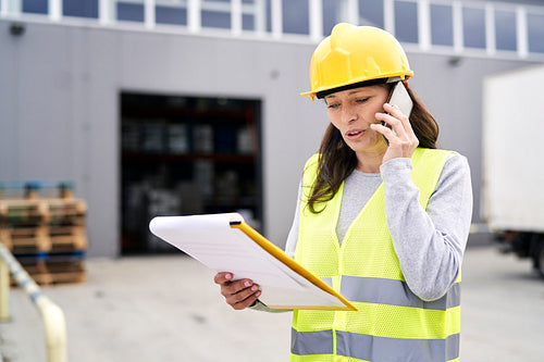 Caucasian mature woman in front of warehouse talking by mobile phone