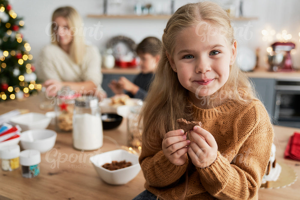 Cute girl eating homemade cookie while sitting on table