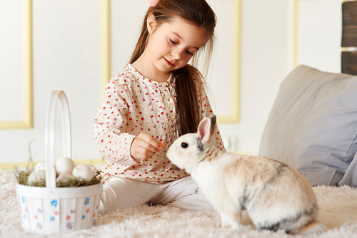 Small girl playing with rabbit on the bed