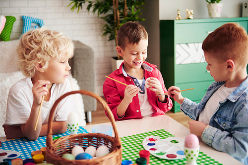 Three happy boys painting easter eggs