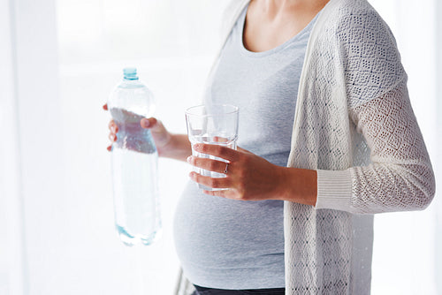 Unrecognizable pregnant woman drinking water
