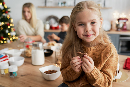 Cute girl eating homemade cookie while sitting on table