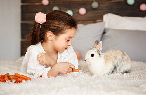 Girl lying on the bed and feeding the rabbit