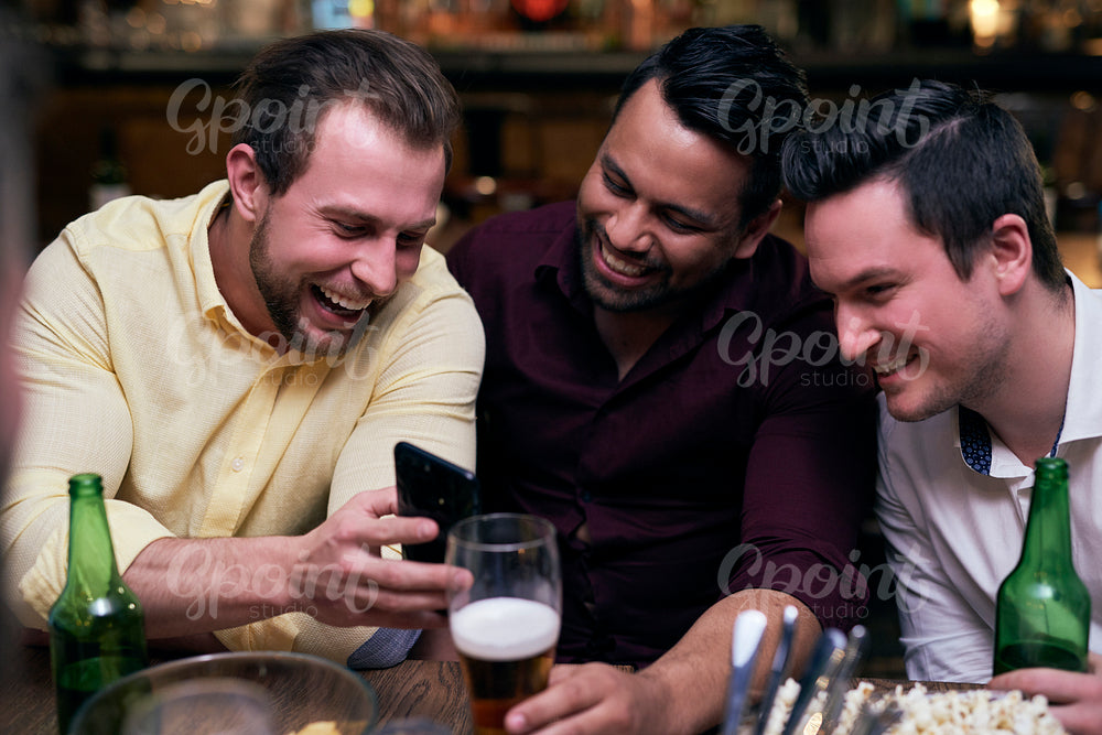Three men using mobile phone during meeting in the pub