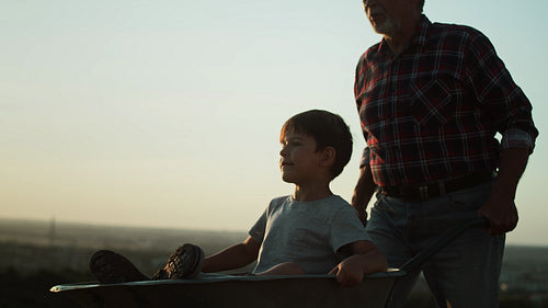 Video of grandfather driving grandson in wheelbarrows at sunset