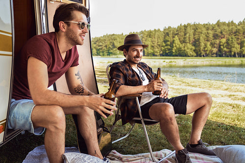 Two young male friends spending time on the camper side and drinking beer
