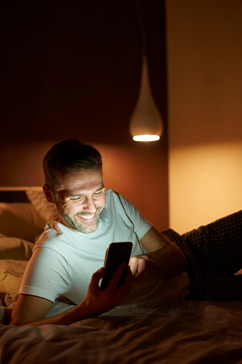 Smiling man using a mobile phone in bed