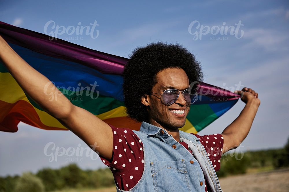Young African man with rainbow flag standing at beach
