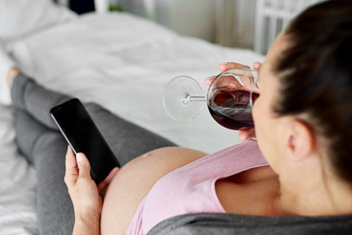 Woman in advanced pregnancy drinking alcohol in bed
