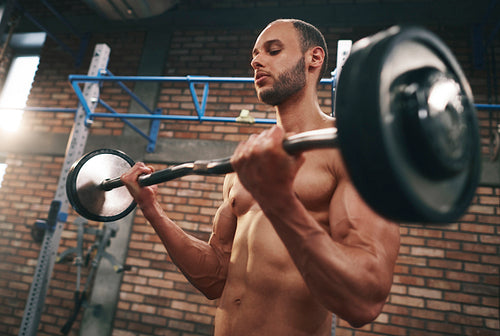 Muscular man lifting barbell in gymnasium