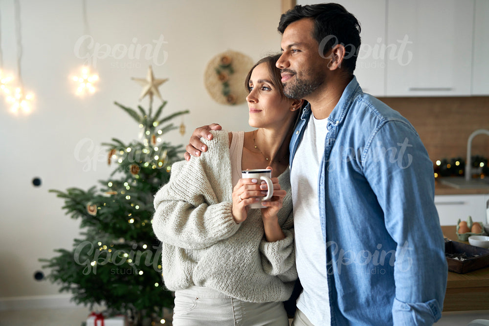 Multi ethnicity couple standing at home at Christmas time and looking away