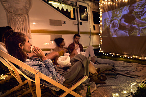 Young cheerful people watching a movie on camping site