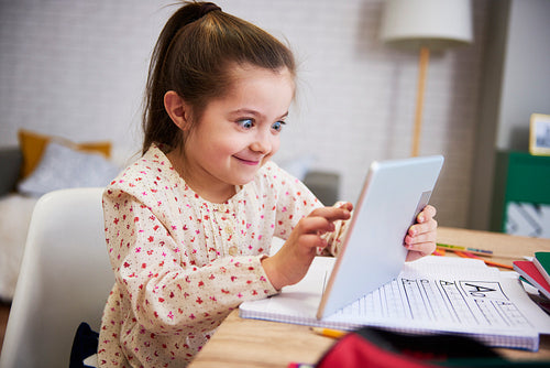 Playful child using a tablet while doing his homework at home