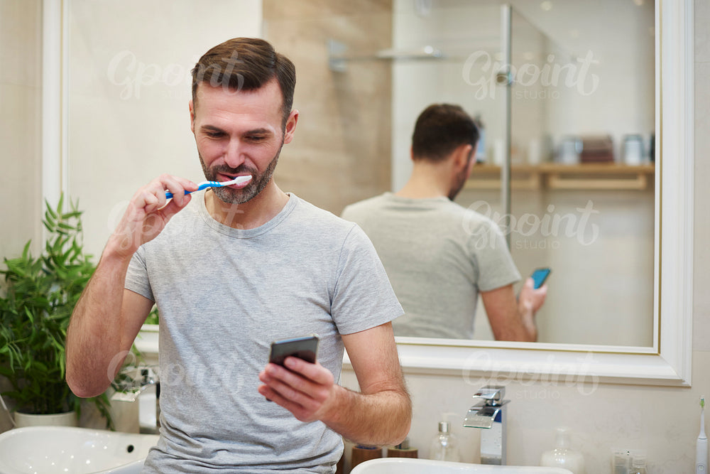 Man brushing his teeth and using mobile phone in bathroom