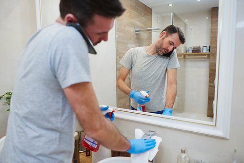 Man cleaning his bathroom and talking by mobile phone