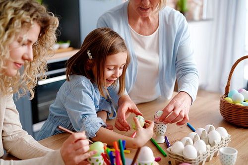 Mother grandmother and granddaughter decorate easter eggs together