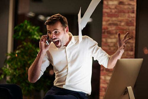 Screaming man talking by mobile phone in office