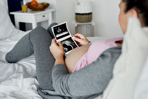 Pregnant woman browsing ultrasound images on bed
