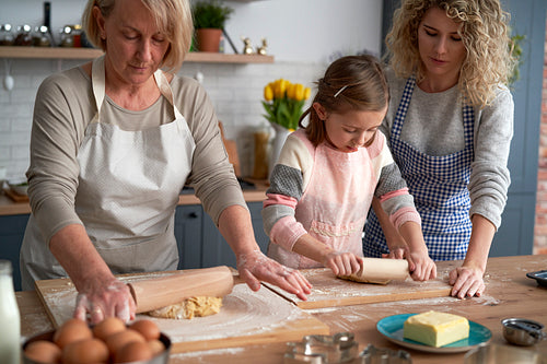 Three generations of women rolling dough together at home